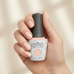 Mano sosteniendo el frasco de esmalte en gel Gelish Simply Irresistible, color Nudes acabado Cream, con las uñas pintadas del mismo tono