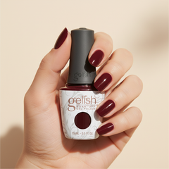 Mano sosteniendo el frasco de esmalte en gel Gelish Wonder Woman, color Rojos acabado Shimmer, con las uñas pintadas del mismo tono