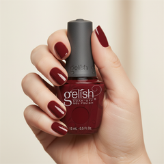Mano sosteniendo el frasco de esmalte en gel Gelish Man Of The Moment, color Rojos acabado Cream, con las uñas pintadas del mismo tono
