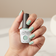 Mano sosteniendo el frasco de esmalte en gel Gelish Mint Chocolate Chip, color Verdes acabado Cream, con las uñas pintadas del mismo tono