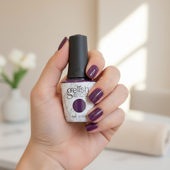 Mano sosteniendo el frasco de esmalte en gel Gelish Tokyo a Go Go, color Morados acabado Cream, con las uñas pintadas del mismo tono