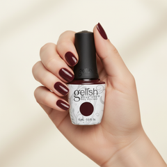 Mano sosteniendo el frasco de esmalte en gel Gelish A Touch Of Sass, color Borgoñas acabado Cream, con las uñas pintadas del mismo tono