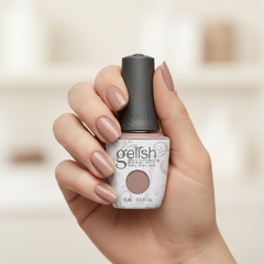 Mano sosteniendo el frasco de esmalte en gel Gelish Tan My Hide, color Nudes acabado Cream, con las uñas pintadas del mismo tono