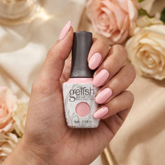 Mano sosteniendo el frasco de esmalte en gel Gelish All About The Pout, color Rosas acabado Cream, con las uñas pintadas del mismo tono