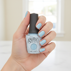 Mano sosteniendo el frasco de esmalte en gel Gelish Not So Prince Charming, color Azules acabado Cream, con las uñas pintadas del mismo tono