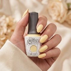 Mano sosteniendo el frasco de esmalte en gel Gelish Let Down Your Hair, color Amarillos acabado Cream, con las uñas pintadas del mismo tono
