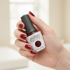 Mano sosteniendo el frasco de esmalte en gel Gelish What's Your Poinsettia?, color Rojos acabado Shimmer, con las uñas pintadas del mismo tono