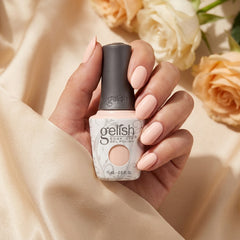 Mano sosteniendo el frasco de esmalte en gel Gelish Barely Buff, color Nudes acabado Cream, con las uñas pintadas del mismo tono