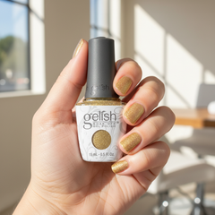 Mano sosteniendo el frasco de esmalte en gel Gelish Star Quality, color Amarillos acabado Glitter, con las uñas pintadas del mismo tono
