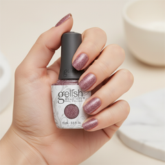 Mano sosteniendo el frasco de esmalte en gel Gelish Mesmerized By You, color Borgoñas acabado Glitter, con las uñas pintadas del mismo tono