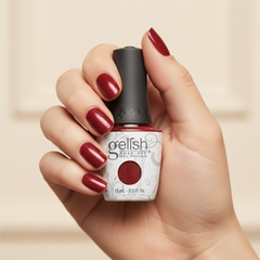 Mano sosteniendo el frasco de esmalte en gel Gelish Hold The Camera, color Rojos acabado Glitter, con las uñas pintadas del mismo tono