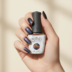 Mano sosteniendo el frasco de esmalte en gel Gelish Aurora - Space Dust, color Azules acabado Cat Eye, con las uñas pintadas del mismo tono