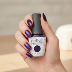 Mano sosteniendo el frasco de esmalte en gel Gelish Aurora - Love At First Light, color Morados acabado Cat Eye, con las uñas pintadas del mismo tono