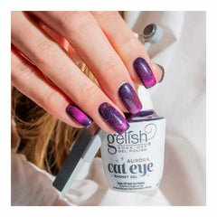 Mano con las uñas en Gelish Aurora Cat Eye Love At First Light, morado profundo con remolino magenta, sosteniendo el frasco Aurora Cat Eye Magnet Gel
