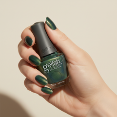 Mano sosteniendo el frasco de esmalte en gel Gelish Aurora - Big Bang For Your Buck, color Verdes acabado Cat Eye, con las uñas pintadas del mismo tono