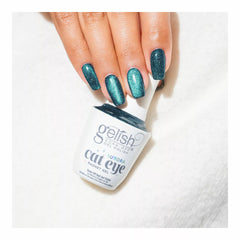 Mano con las uñas en Gelish Aurora Cat Eye Come Sky With Me, azul petróleo oscuro con remolino azul, sosteniendo el frasco Aurora Cat Eye Magnet Gel