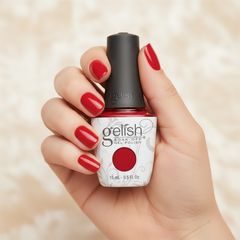 Mano sosteniendo el frasco de esmalte en gel Gelish Fire Cracker, color Rojos acabado Cream, con las uñas pintadas del mismo tono