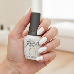 Mano sosteniendo el frasco de esmalte en gel Gelish Sheek White, color Blancos acabado Cream, con las uñas pintadas del mismo tono