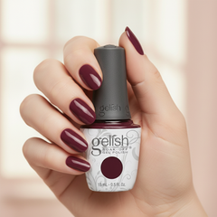 Mano sosteniendo el frasco de esmalte en gel Gelish Stand Out, color Borgoñas acabado Cream, con las uñas pintadas del mismo tono