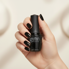 Mano sosteniendo el frasco de esmalte en gel Gelish Black Shadow, color Negros acabado Cream, con las uñas pintadas del mismo tono