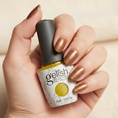 Mano sosteniendo el frasco de esmalte en gel Gelish Bronzed, color Amarillos acabado Glitter, con las uñas pintadas del mismo tono