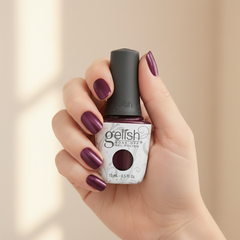 Mano sosteniendo el frasco de esmalte en gel Gelish Samurai, color Morados acabado Shimmer, con las uñas pintadas del mismo tono