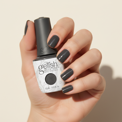 Mano sosteniendo el frasco de esmalte en gel Gelish Midnight Caller, color Negros acabado Shimmer, con las uñas pintadas del mismo tono