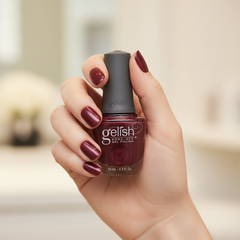 Mano sosteniendo el frasco de esmalte en gel Gelish Rose Garden, color Rojos acabado Shimmer, con las uñas pintadas del mismo tono