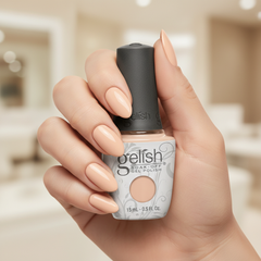 Mano sosteniendo el frasco de esmalte en gel Gelish Need a Tan, color Nudes acabado Cream, con las uñas pintadas del mismo tono