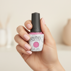 Mano sosteniendo el frasco de esmalte en gel Gelish It's a Lily, color Rosas acabado Cream, con las uñas pintadas del mismo tono
