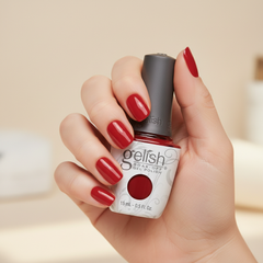 Mano sosteniendo el frasco de esmalte en gel Gelish Hot Rod Red, color Rojos acabado Cream, con las uñas pintadas del mismo tono