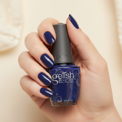 Mano sosteniendo el frasco de esmalte en gel Gelish After Dark, color Azules acabado Cream, con las uñas pintadas del mismo tono