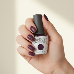 Mano sosteniendo el frasco de esmalte en gel Gelish Plum And Done, color Borgoñas acabado Cream, con las uñas pintadas del mismo tono