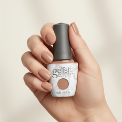 Mano sosteniendo el frasco de esmalte en gel Gelish Taupe Model, color Nudes acabado Cream, con las uñas pintadas del mismo tono