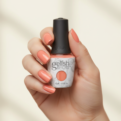 Mano sosteniendo el frasco de esmalte en gel Gelish Sweet Morning Dew, color Naranjas acabado Cream, con las uñas pintadas del mismo tono