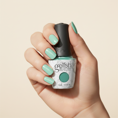 Mano sosteniendo el frasco de esmalte en gel Gelish A Mint Of Spring, color Verdes acabado Cream, con las uñas pintadas del mismo tono