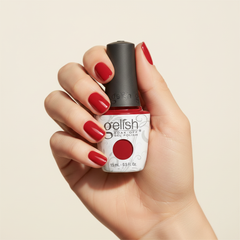 Mano sosteniendo el frasco de esmalte en gel Gelish Shake It Till You Samba, color Rojos acabado Cream, con las uñas pintadas del mismo tono