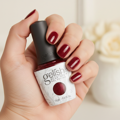Mano sosteniendo el frasco de esmalte en gel Gelish All Tied Up¿ With a Bow, color Rojos acabado Shimmer, con las uñas pintadas del mismo tono