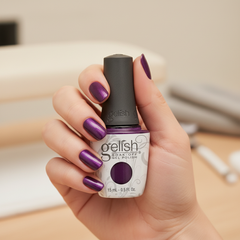 Mano sosteniendo el frasco de esmalte en gel Gelish You Glare I Glow, color Morados acabado Cream, con las uñas pintadas del mismo tono