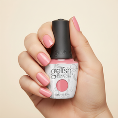 Mano sosteniendo el frasco de esmalte en gel Gelish Make You Blink Pink, color Rosas acabado Cream, con las uñas pintadas del mismo tono