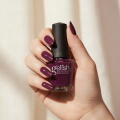 Mano sosteniendo el frasco de esmalte en gel Gelish Love Me Like a Vamp, color Borgoñas acabado Cream, con las uñas pintadas del mismo tono