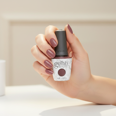 Mano sosteniendo el frasco de esmalte en gel Gelish Lust At First Sight, color Mauves acabado Cream, con las uñas pintadas del mismo tono