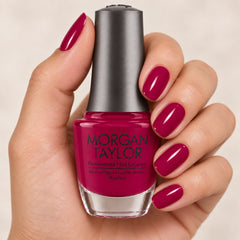 Mano sosteniendo el frasco de esmalte tradicional Morgan Taylor La la Love You!, color Rosas acabado Cream, con las uñas pintadas a juego