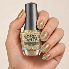 Mano sosteniendo el frasco de esmalte tradicional Morgan Taylor Grand Jewels, color Blancos acabado Glitter, con las uñas pintadas a juego