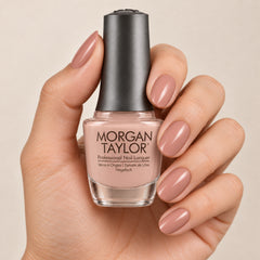 Mano sosteniendo el frasco de esmalte tradicional Morgan Taylor Do I Look Buff?, color Nudes acabado Cream, con las uñas pintadas a juego