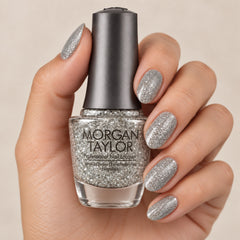 Mano sosteniendo el frasco de esmalte tradicional Morgan Taylor Am I Making You Gelish?, color Blancos acabado Glitter, con las uñas pintadas a juego