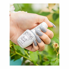 Mano con uñas plateadas con glitter sosteniendo el frasco Gelish Flash Glam Dripping In Bling al aire libre