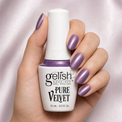 Mano sosteniendo el frasco de esmalte en gel Gelish Cat Eye Pure Velvet Pull Me In, color Morados acabado Cat-eye, con las uñas pintadas del mismo tono