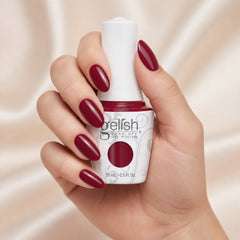 Mano sosteniendo el frasco de esmalte en gel Gelish Hello, Merlot!, color Borgoñas acabado Cream, con las uñas pintadas del mismo tono