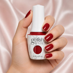 Mano sosteniendo el frasco de esmalte en gel Gelish Red Roses, color Rojos acabado Cream, con las uñas pintadas del mismo tono